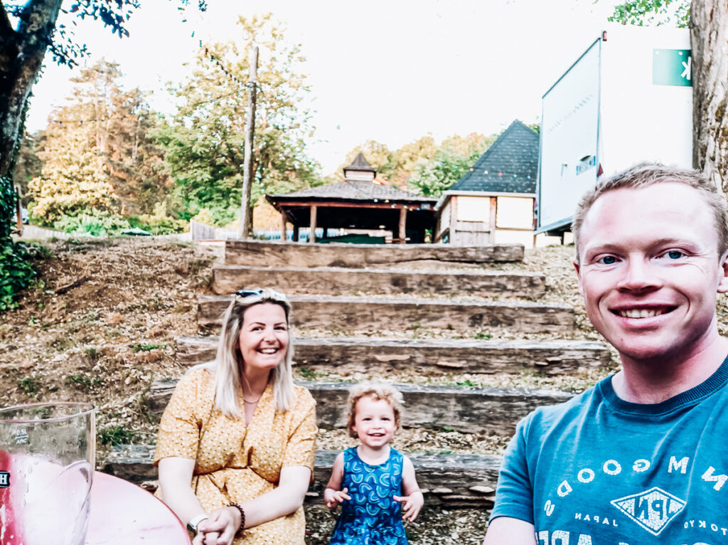 3 memebers of a family sitting on a set of steps outside the bar area of Huttopia sarlat campsite