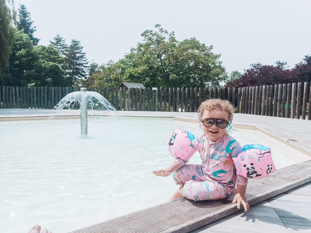 sassy toddler with armbands on sat outside the toddler splash pool at sarlat huttopia