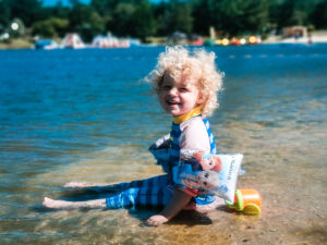 The toddler from family camping europe wearing frozen armbands and sitting in the lake at camping sandaya les alicourts