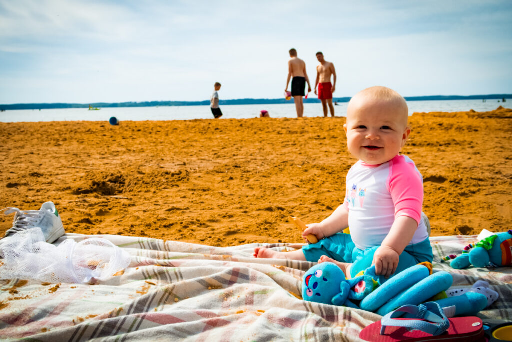 tODDLER SITTING ON A SANDY LAKE BEACH AT LA RIVE CAMPSITE ONE OF THE BEST CHILD FRIENDLY CAMPSITES IN FRANCE