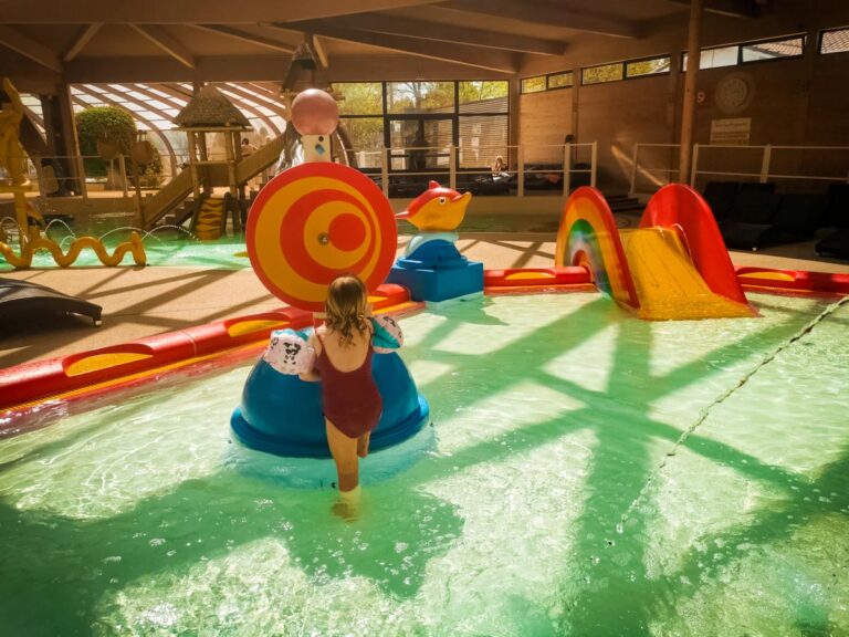 A child playing in an indoor splash pool with a target ring slide, Yelloh Village La Rive