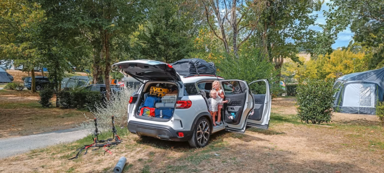 A car full of family camping equipment with two children standing on the car doorway the car is parked on a camping emplacement and a campsite in france